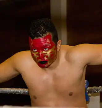 Un catcheur brun torse nu au visage peint en rouge et en jaune or.