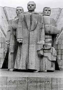 Photo noir et blanc montrant une sculpture en pierre de trois hommes debout, titrée « Klement Gottwald ».