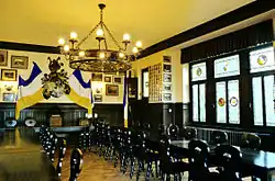 Les murs sont décorés des armes et des couleurs de la société ainsi que des photos encadrées. Les tables sont disposées en U sont entourées de chaises. Les boiseries et les meubles en bois sombre, les fenêtres comportent de petits vitraux avec les armes.