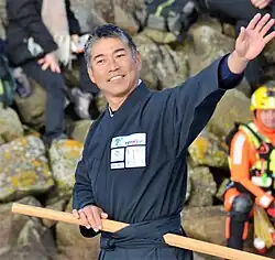 Dans le chenal des Sables-d'Olonne, en buste, souriant, il salue la foule. Il est vêtu d'un kimono gris sombre et porte un sabre de bois à la ceinture.