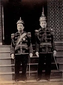 Photographie de deux hommes debout faisant face au photographe. Ils portent des uniformes militaires de cérémonie.
