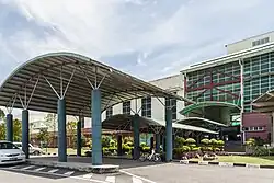 Photographie d'un grand bâtiment vitré et de ses trois portiques ombragés.