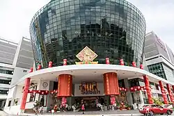 Photographie d'un grand bâtiment vitré cylindrique décoré aux couleurs de la Chine. Sur sa devanture il est inscrit « Suria Sabah ».