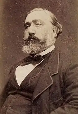 Photo en noir et blanc d'un homme bedonnant d'âge mûr, assis et de trois-quarts.