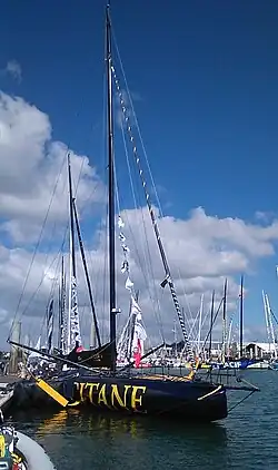 Vu de trois quarts avant, voilier noir à décoration or, amarré au ponton.