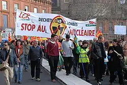 Photo couleur de manifestants défilant dans une rue et portant une banderole blanche sur laquelle on peut lire « Stop au nucléaire ».