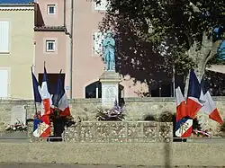Une statue de Poilu peinte monte la garde sur un socle carré. Monument pavoisé pour le 11 novembre
