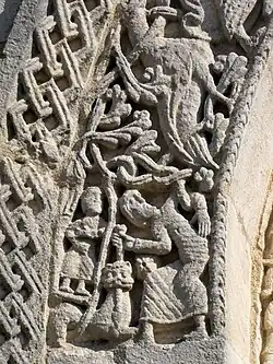 À gauche, un homme debout poignarde la tête d'un lion, et un autre personnage dans un cartouche fait de tiges. Au-dessus, un griffon ou un aigle