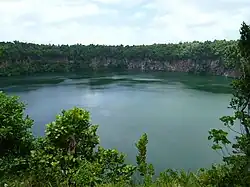photo d'une partie du lac, entouré de falaises et bordé par des arbustes au premier plan.