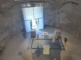 Vue intérieure du temple de Romulus, depuis la verrière située dans la basilique Santi Cosma e Damiano (ancien vestibule de la basilique). En 2015, le temple accueille la reconstruction du mobilier de la fontaine de Juturne (Fons Iuturnae).