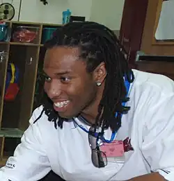 Larry Fitzgerald, un homme noir, avec des tresses, un t-shirt blanc et une boucle d'oreille, sourit à des supporters.