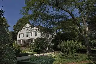 Photographie couleur d'un vaste demeure à façade blanche, au fond d'un parc