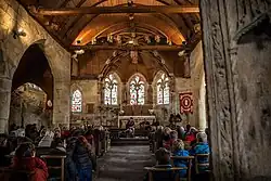 Au fond, les trois fenêtres de l'abside. Vue sur une partie de la voûte lambrissée : au-dessus de l'abside, de la croisée du transept et du début de la nef. Deux poutres traversent la nef. Des monstres sculptés semblent les avaler. À gauche, on voit la première arcade.