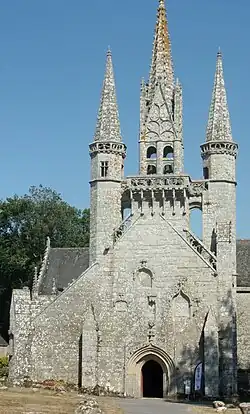 Façade dissymétrique d'une chapelle surmontée d'un clocher encadré de deux tourelles, un peu moins hautes que lui, et qui ont toutes deux une flèche, comme lui. Elles sont reliées au clocher par deux passerelles.