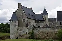 Photographie en couleurs d'un pont franchissant des douves, un muraille et des anciens bâtiments venant le cerner de part et d'autre.