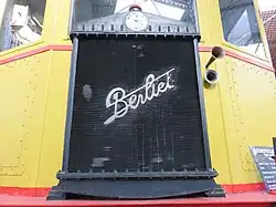 Photographie en couleurs montrant la calandre du radiateur avant de l'autorail, le petit logo de Berliet représente une locomotive à vapeur américaine vue de face sur un fond bleu clair.