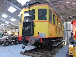 Photographie en couleurs montrant une vue de trois quarts avant de l’autorail, livrée jaune avec liserés rouges.