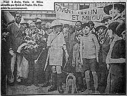 Photographie extraite d'un journal et montrant un jeune garçon accompagné d'un chien et entouré d'une foule nombreuse.
