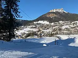 Domaine de ski alpin enneigé, téléski, village enneigé, dominé par le sommet de Chamechaude, le tout sous le soleil et le ciel bleu.