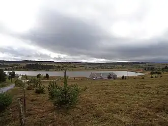 Photographie couleur d'un lac de montagne entouré de prairies et de forêts