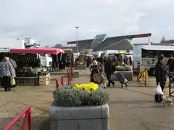 Photographie en couleurs d'un marché en extérieur, une vasque fleurie au premier plan.