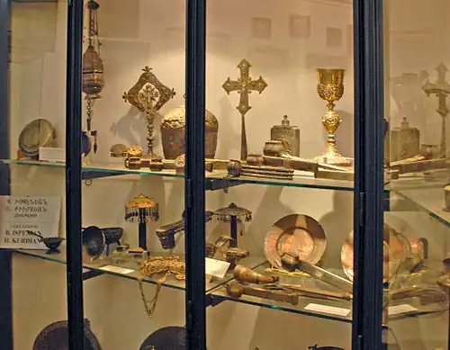 Photographie couleur d'une vitrine présentant des croix, des calices et d'autres objets sacrés, en métal dont certains dorés.