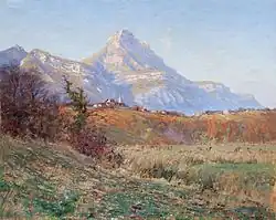 Sur un coteau aux couleurs automnales, un village avec un clocher est dominé en arrière-plan par une montagne.