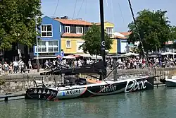 Vu de trois quarts arrière, en entier, voilier noir et argenté, amarré au quai.