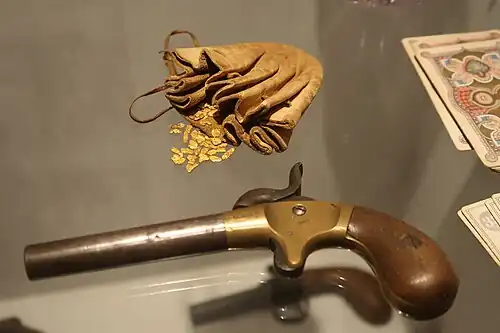 Bourse en cuir et pépites d'or fluviales (XIXe&nbsp;siècle). Petit pistolet de jeu à un coup (vers 1850), acier, laiton, bois. Cartes à jouer.