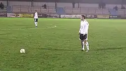 Photographie d'un joueur, portant un maillot blanc, s'apprêtant à tirer un coup franc.