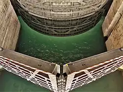 Vue plongeante sur une espèce de sas gardé par une porte à battants plats d'un coté, et une porte à battant rond de l'autre ; au fond une eau verte.
