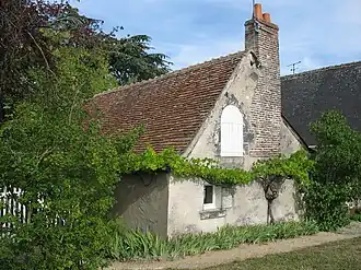 Photographie en couleurs et vue de trois-quarts d'une maison en pierres de taille de couleur beige et à toit aux pentes douces, la couverture d'un corps de logis visible en arrière-plan.