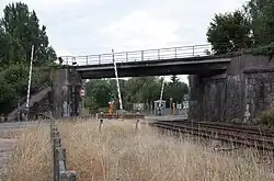 Vue du tablier d'un pont, au-dessus d'un passage à niveau (barrières levées), par temps nuageux.