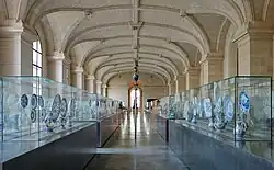 Vue de la galerie en enfilade bordée de vitrines présentant les pièces.