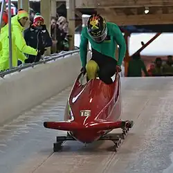 Vue d'un homme en combinaison verte entrant dans un bobsleigh rouge