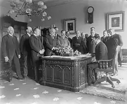Le secrétaire d'État John Hay signe un traité de paix avec l'Espagne sur le Resolute desk dans le bureau du président McKinley, alors situé au 1er&nbsp;étage de la résidence exécutive de la Maison-Blanche (actuelle Lincoln Bedroom) c. 1899.