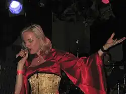 Image d'une femme blonde habillée d'un haut à grande manche rouge et d'un corset jaune chantant dans un micro