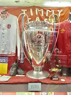 Grande coupe argentée présentée au milieu d'autres souvenirs dans une vitrine de musée.