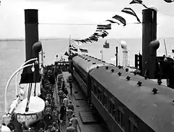 photographie en noir et blanc d'un train transbordé par un ferry sur un fleuve.