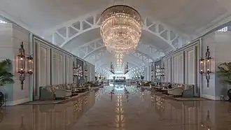 Vue symétrique du spacieux hall salon avec sofas et énorme luminaire se réfléchissant au sol, à l'hôtel The Fullerton Bay, Singapour. Juin 2018.