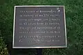 Photo agrandie d'une plaque commémorative noir avec un texte en blanc surplombant une pelouse.