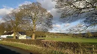 Photographie couleur d'un champ situé en bord de route, sur les franges duquel des bâtiments sont bâtis.