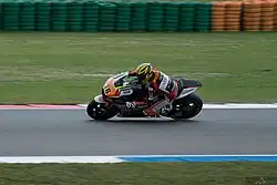 Vue de profil, d'une moto et son pilote fans un virage, la moto se dirigeant vers la gauche de la photo.