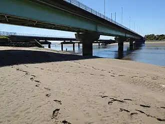 Photo d'un pont vu d'en bas depuis un banc de sable avec plusieurs empreintes de pas.