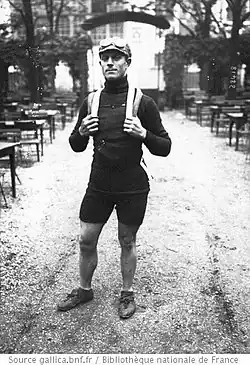 Photographie en noir et blanc d'un coureur cycliste, debout.