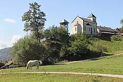 vu du village avec à l'avant plan une prairie et un cheval, et derrière un château d'eau et une église blanche.