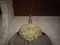Gros plan sur un petit lustre ouvragé de l'une des nefs secondaires de la salle de prière. Il présente un plateau circulaire finement ajouré, surmonté de merlons en dents de scie.