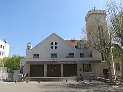 Église du XXe&nbsp;siècle. Clocher une tour octogonale sur le côté surmontée d'une croix domine un parvis.