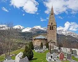 Photo de l'édifice avec au premier plan des pierres tombales et en arrière plan une série de sommets partiellement enneigés.