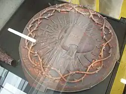 Photo : médaillon en métal en haut-relief d'un cœur rayonnant surmonté d'une croix et double tresse d'épines en bordure.